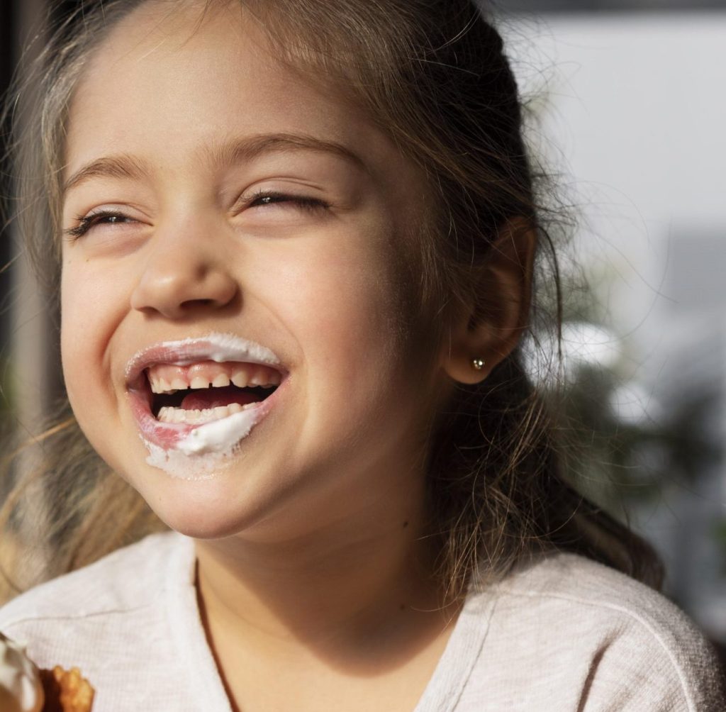 Une petite fille au grand sourire, qui mange une glace